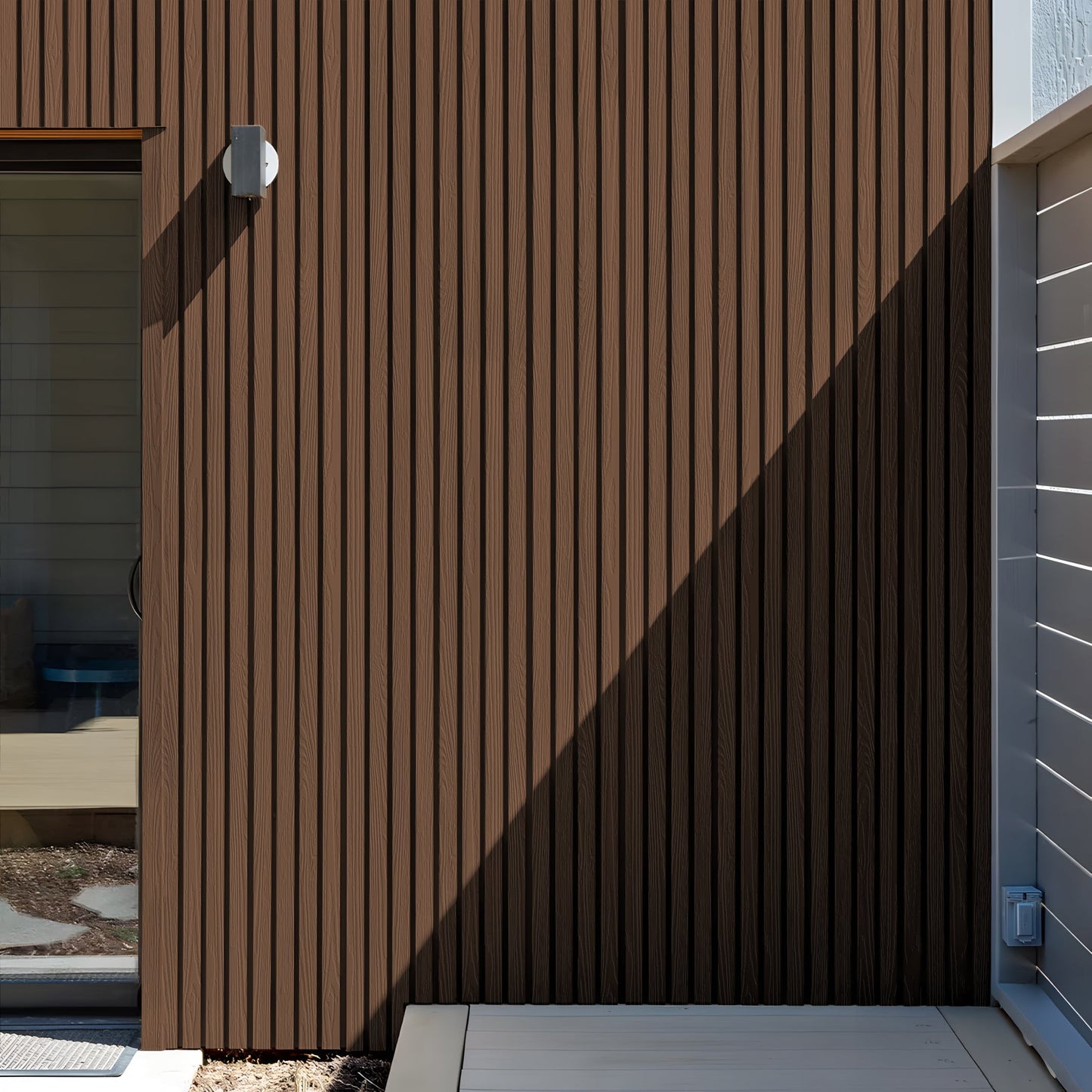 A Burnt Caramel Exterior WPC Panel by Landmark Decor features brown vertical slats, weather-resistant panels, a light fixture, partial glass door, and a distinct shadow sharply dividing sunlight and shade.
