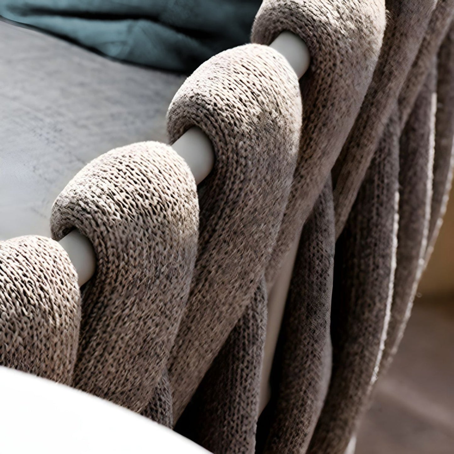 A close-up of a Coastal Woven Collection blanket by Landmark Decor, draped over a railing. Its light beige chunky knit and twisted pattern provide cozy vibes, ideal for alfresco dining. Sunlight enhances its inviting warmth and soft texture.
