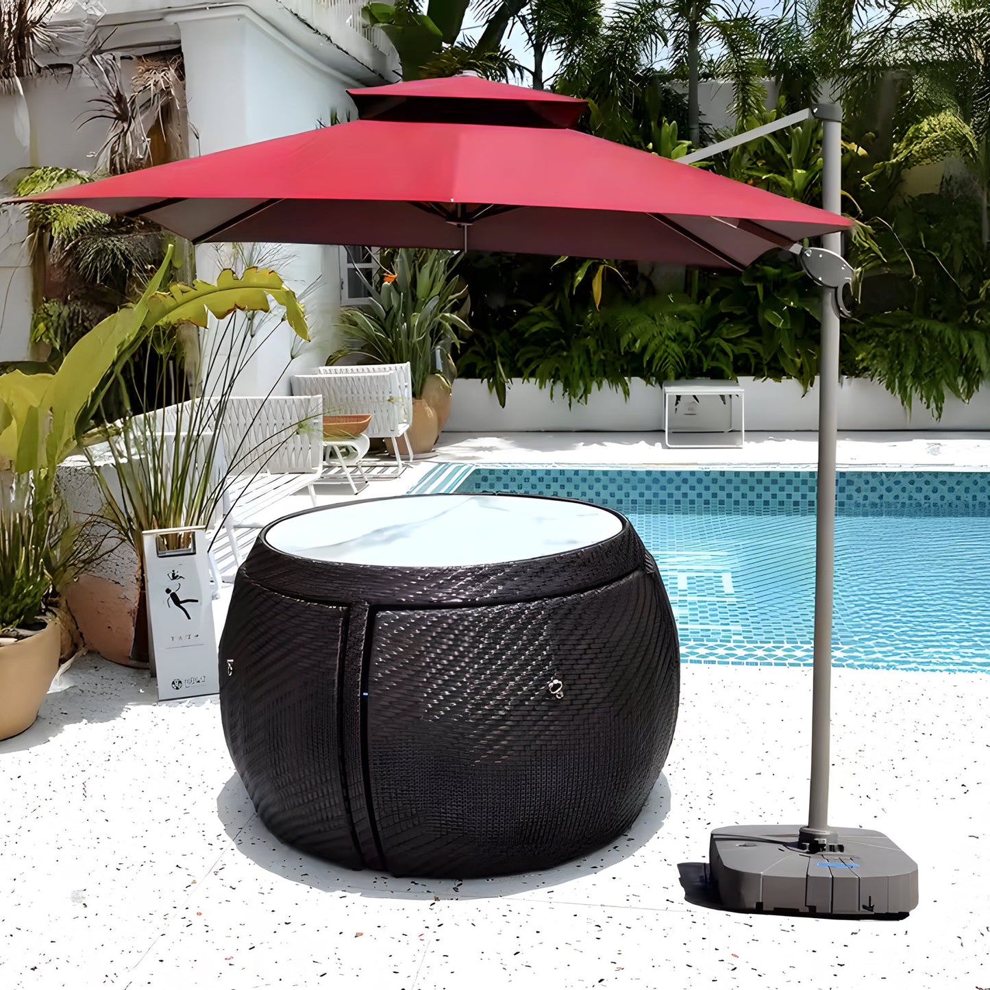 A poolside scene showcases the Midnight Riviera Collection from Landmark Decor, with a round rattan table and glass top for alfresco dining under a red umbrella. Surrounded by potted green plants and adjacent to a blue-tiled pool, the setting uses weather-resistant materials for lasting enjoyment.