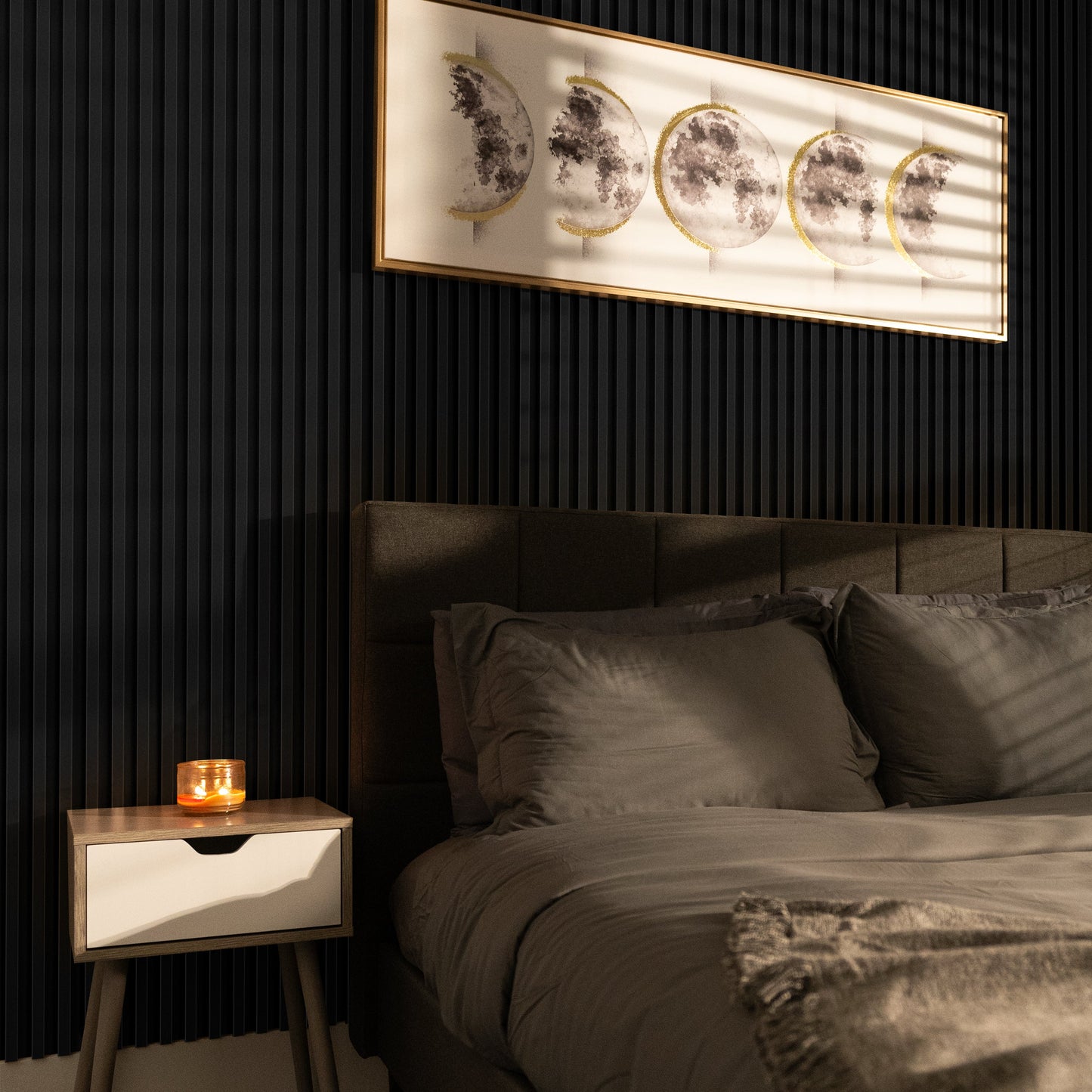A modern bedroom with a grey bed, wooden nightstand with a lit candle, and moon phase art on dark accent walls featuring Landmark Decor’s Absolute Noir WPC Fluted Slat Wall Panel.