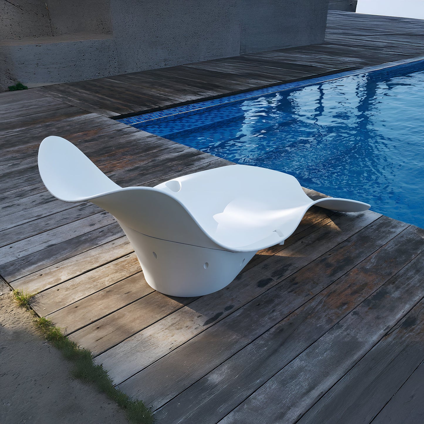 The Muse Astratta Lounger by Landmark Decor graces the wooden deck beside a blue pool, creating a luxurious retreat. Its modern sculptural design, with sleek white curves, embodies outdoor living, offering a striking contrast to the natural wood and shimmering water.