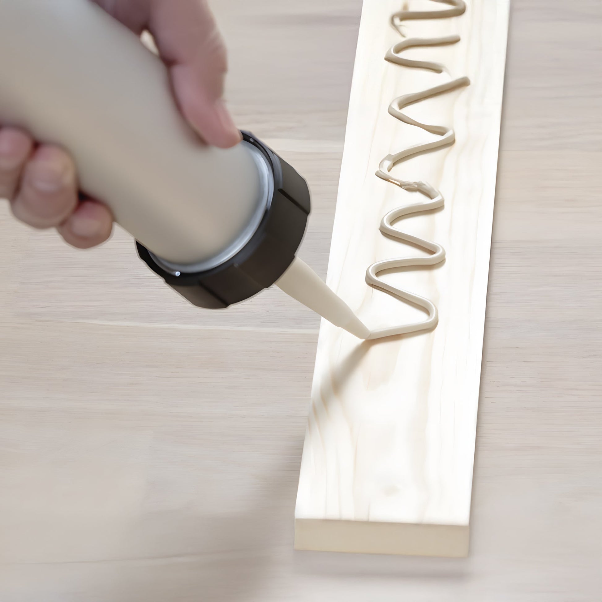 A person uses a caulking gun to apply Landmark Decor Wall Panel Installation Adhesive in a zigzag pattern on a wooden board, prepping it for decorative wall panels or installation.