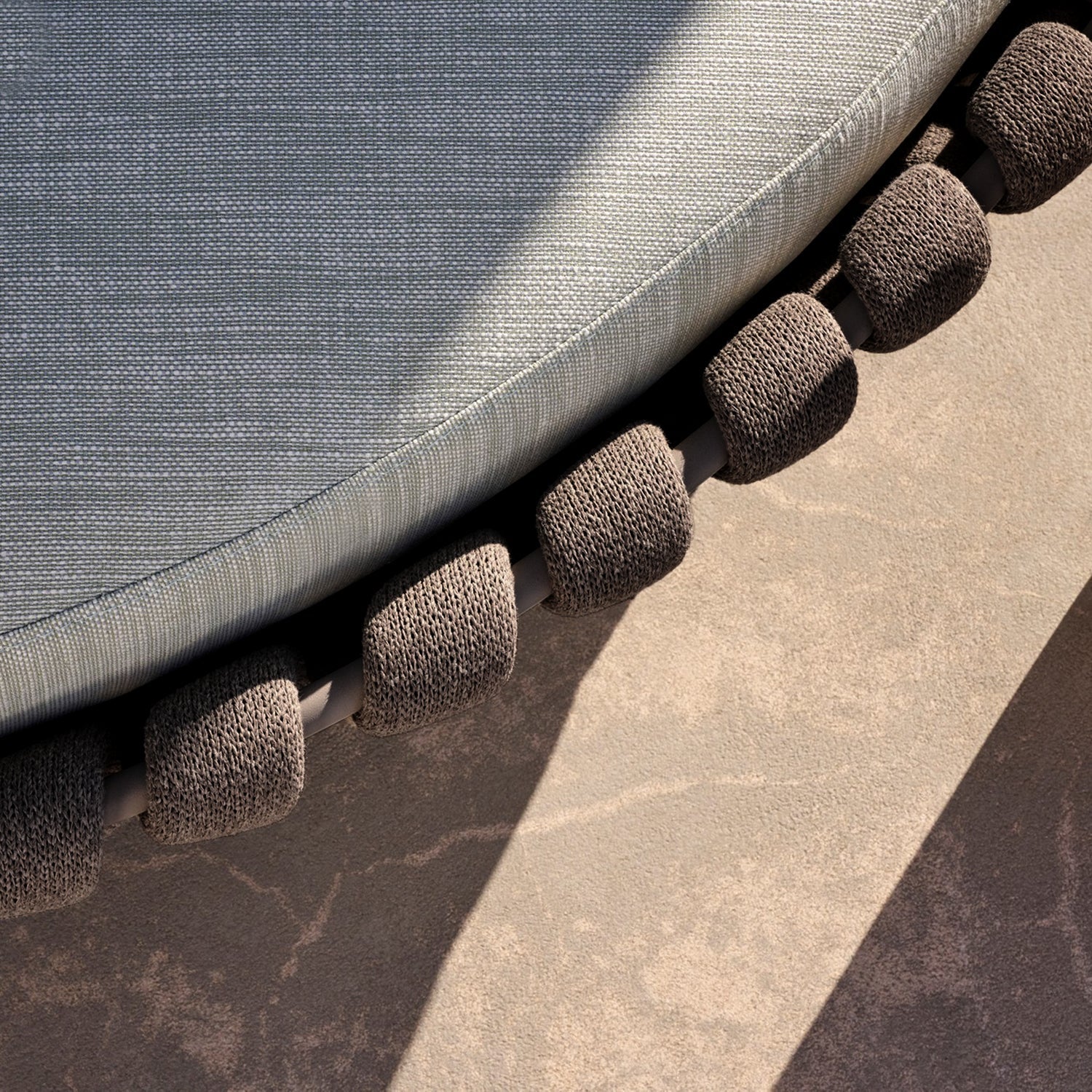A close-up of a trampoline edge with curved foam padding around the springs casts shadows onto the textured concrete below, encapsulating outdoor living. This scene beautifully complements nearby Mediterranea Luxe Lounges by Landmark Decor in this luxurious retreat.