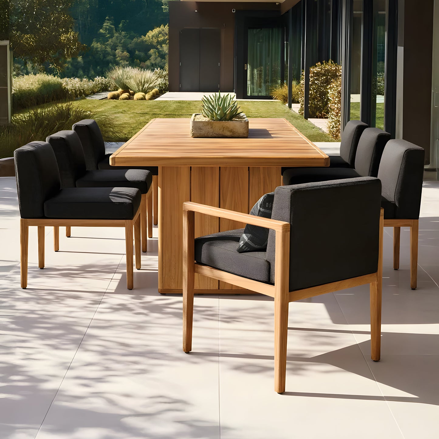 The alfresco dining area showcases Landmark Decors Sienna Terrace Collection, featuring a wooden table with six cushioned chairs on a tiled patio. A succulent centerpiece adorns the table as sunlight creates leaf-patterned shadows, highlighting the weather-resistant materials amid greenery and a modern building backdrop.