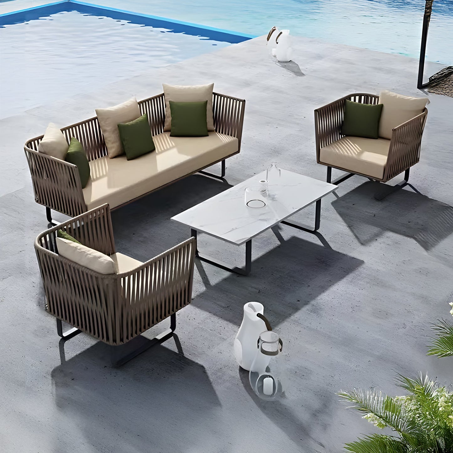 The outdoor lounge boasts the Sierra Luxe Collection by Landmark Decor with a wicker sofa, two armchairs with beige and green weather-resistant cushions, a white rectangular table, and two decorative vases, all overlooking a shimmering blue pool—ideal for relaxation in style.