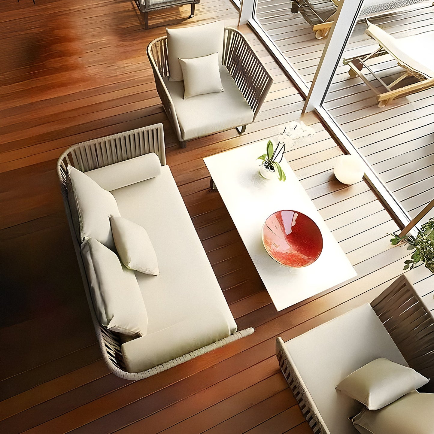 The Sierra Luxe Collection by Landmark Decor showcases an aerial view of a modern, minimalist patio with weather-resistant outdoor sofas encircling a white coffee table with a red bowl. The wooden floor leads to a deck visible through large glass doors, featuring loungers on all-weather frames.