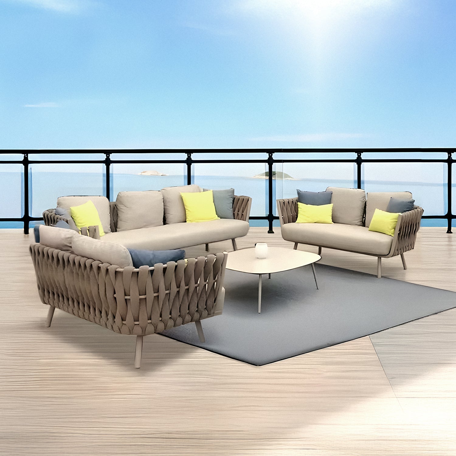 The outdoor terrace showcases the Landmark Decor Elysian Breeze Collection, featuring two beige sofas with weather-resistant yellow and green cushions, a triangular coffee table on a gray rug. A railing offers a view of the calm blue sea under a clear sky.