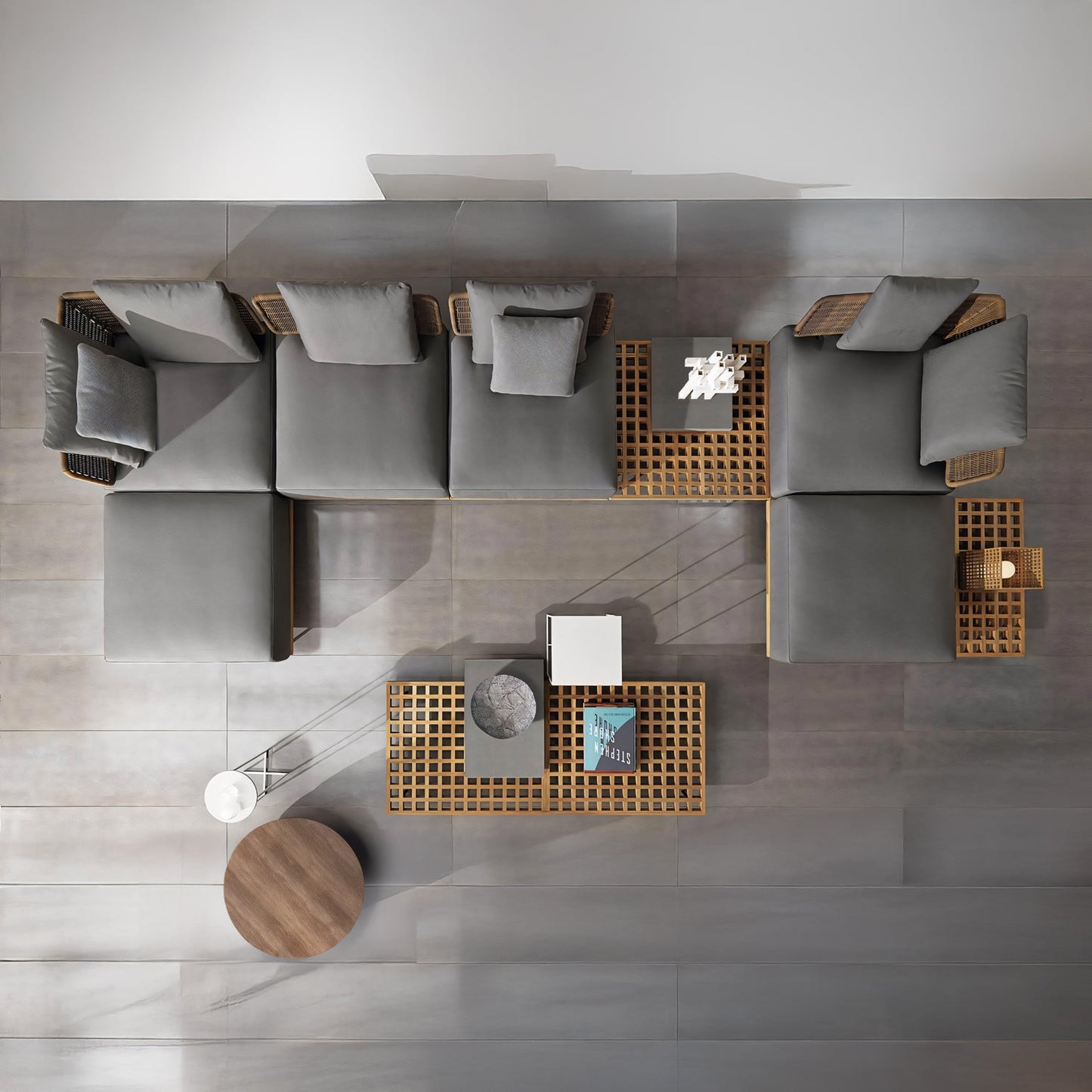 The Oceanview Oasis Collection by Landmark Decor features a modern setup with a gray sectional sofa with weather-resistant cushions, grid-style coffee tables, a round wooden side table, and decorative items like books and small sculptures—ideal for transitioning to an outdoor setting.