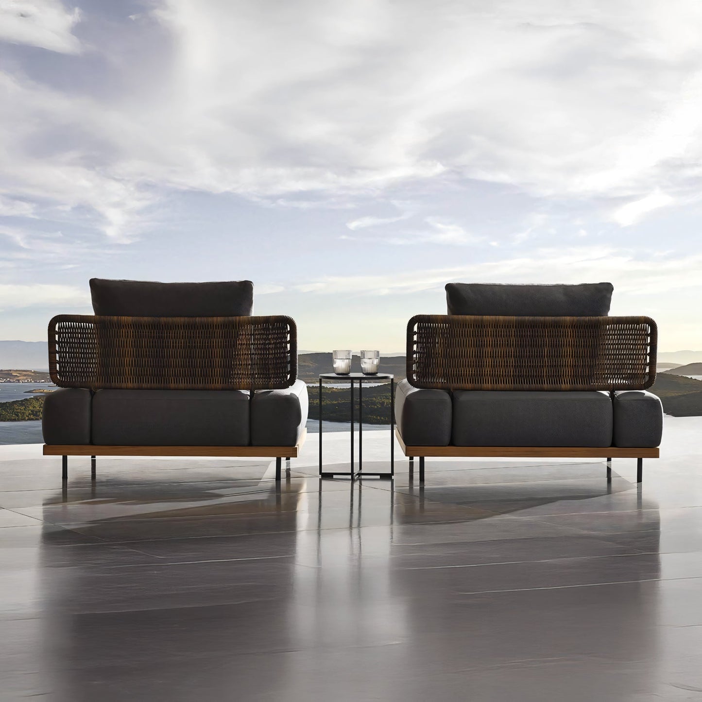 Two wicker and cushioned lounge chairs from the Oceanview Oasis Collection by Landmark Decor feature weather-resistant cushions, facing a mountain view and cloudy sky. A small table with candles completes the setting on the glossy patio floor, creating a perfect space for relaxation.