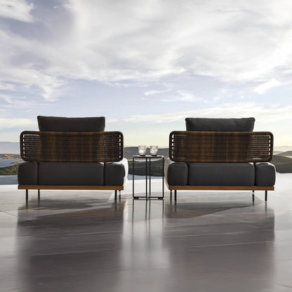 Two wicker and cushioned lounge chairs from the Oceanview Oasis Collection by Landmark Decor feature weather-resistant cushions, facing a mountain view and cloudy sky. A small table with candles completes the setting on the glossy patio floor, creating a perfect space for relaxation.