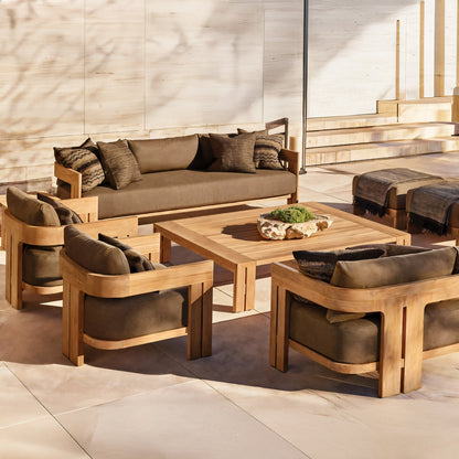 Outdoor patio showcasing the Golden Horizon Collection by Landmark Decor, featuring a wooden furniture set with weather-resistant dark brown cushions. Includes a large sofa, four armchairs, and a square coffee table adorned with a decorative piece amidst sunny light wood and stone surroundings.
