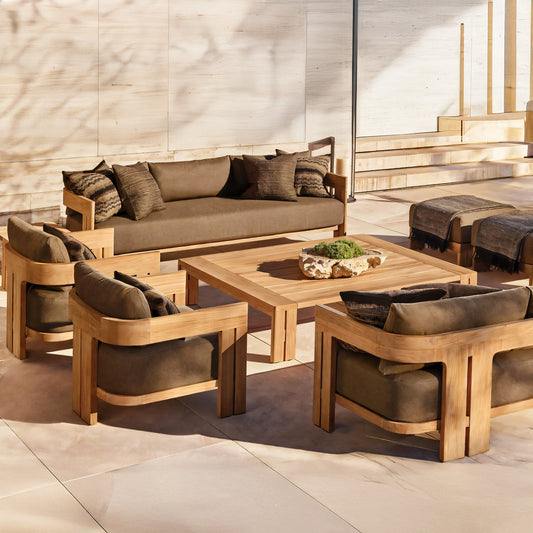 Outdoor patio showcasing the Golden Horizon Collection by Landmark Decor, featuring a wooden furniture set with weather-resistant dark brown cushions. Includes a large sofa, four armchairs, and a square coffee table adorned with a decorative piece amidst sunny light wood and stone surroundings.