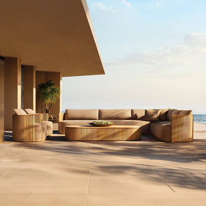 The Coastal Harmony collection by Landmark Decor includes minimalist outdoor furniture with luxurious weather-resistant sofas and a round coffee table. The setting features ocean views, partial shade, a clear blue sky, and is complemented by a nearby potted tree for an idyllic ambiance.