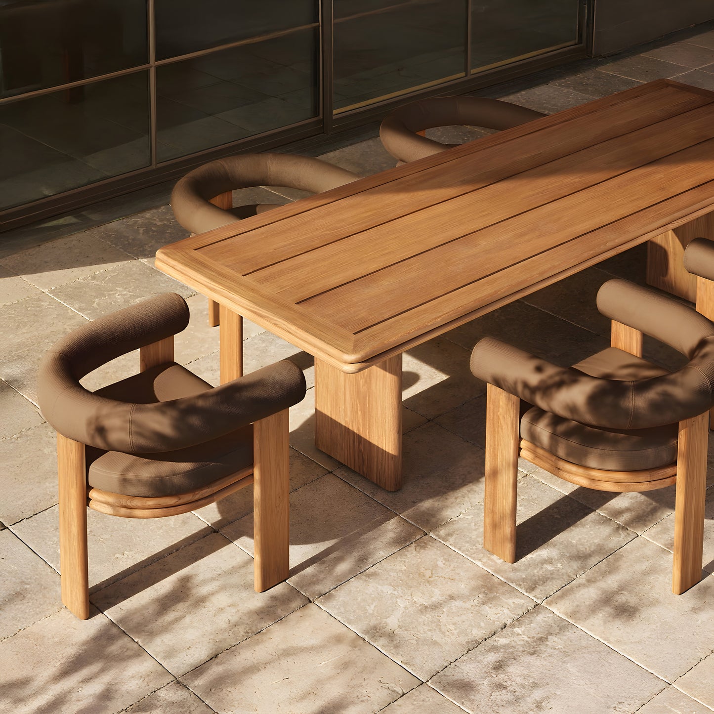 The Amber Ridge Collection by Landmark Decor, featuring a wooden dining table with four cushioned chairs, graces a sunlit stone patio. Shadows of trees dance over this weather-resistant set, creating an inviting alfresco dining experience.