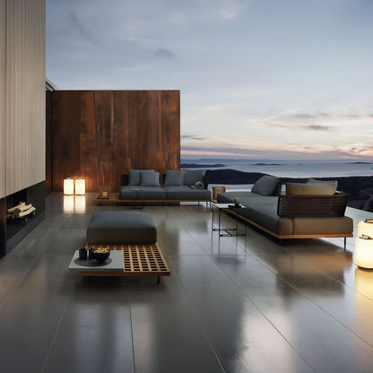 The Oceanview Oasis Collection by Landmark Decor offers sleek gray seating with wooden tables against a wooden accent wall. Weather-resistant cushions and lanterns complete the contemporary look, creating a serene setting with scenic sunset views over hills and water.