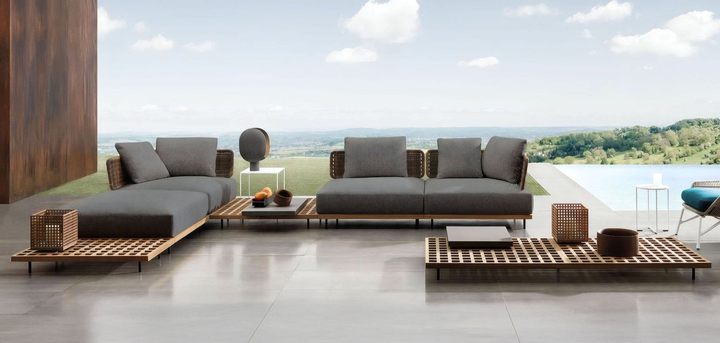 The outdoor patio features the Oceanview Oasis Collection by Landmark Decor, including modern furniture with weather-resistant cushions on a wooden deck overlooking a scenic landscape. This serene setting includes outdoor sofas, a coffee table with decor, and an infinity pool under a partly cloudy sky.