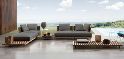The outdoor patio features the Oceanview Oasis Collection by Landmark Decor, including modern furniture with weather-resistant cushions on a wooden deck overlooking a scenic landscape. This serene setting includes outdoor sofas, a coffee table with decor, and an infinity pool under a partly cloudy sky.
