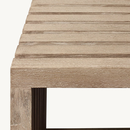 A close-up of the Golden Coast Lounger Set by Landmark Decor highlights its wooden table corner with slatted planks and natural wood grain. The modern design seamlessly enhances outdoor living spaces, offering luxury with minimalist straight edges and visible craftsmanship.