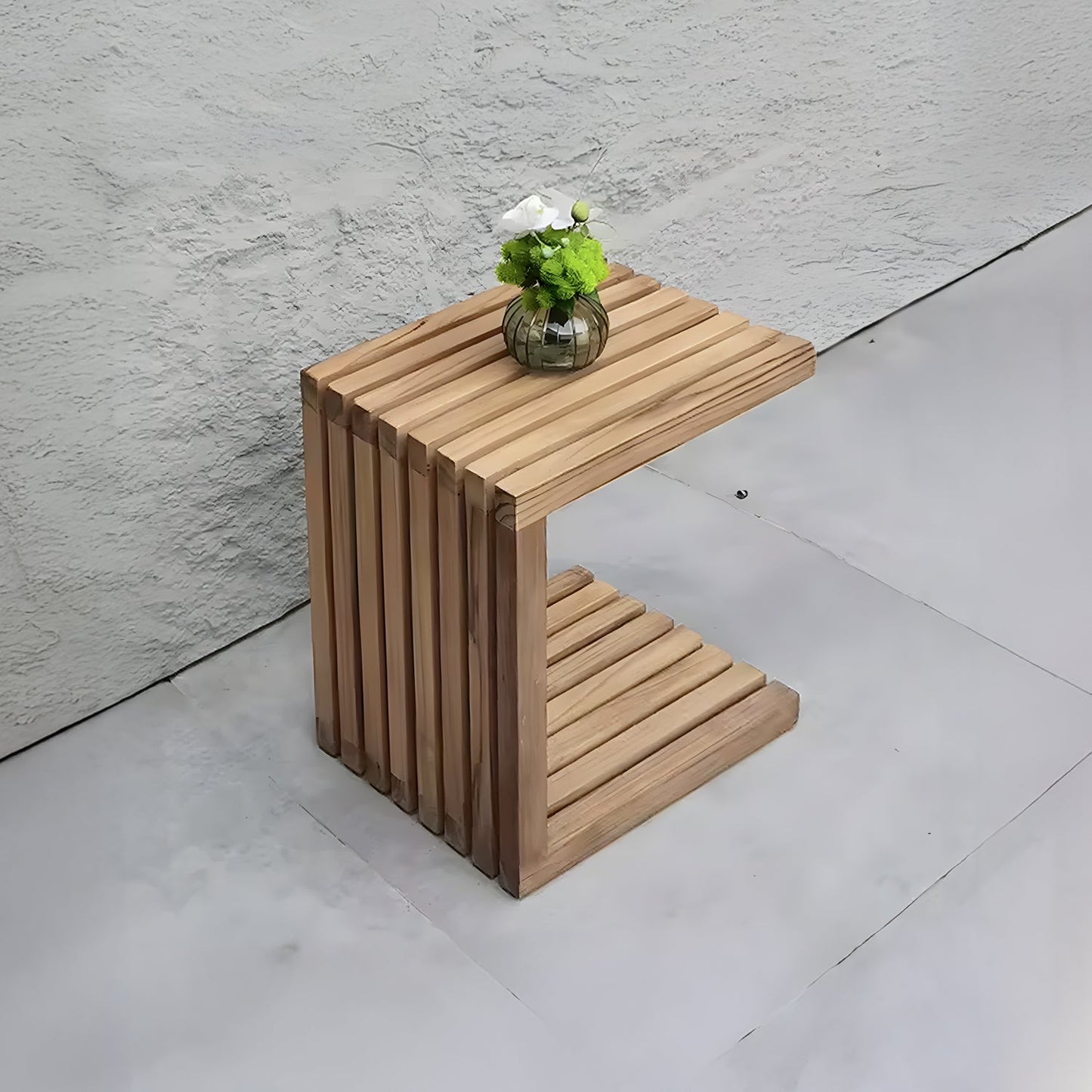 The Golden Coast Lounger Set by Landmark Decor includes a modern wooden side table with a unique slatted design, complementing a small round vase of white and green flowers. Perfect for an outdoor living vibe, it stands against a textured light gray wall on a smooth floor.