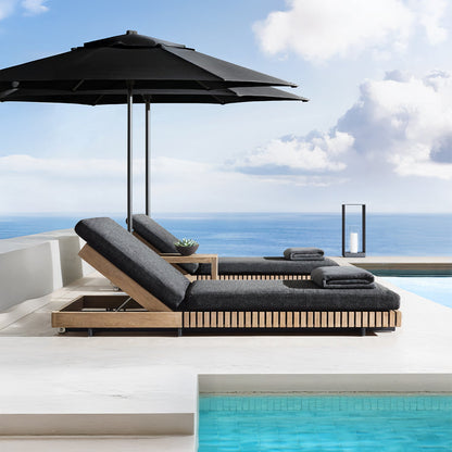 Experience luxury at the modern outdoor poolside, featuring Landmark Decors Golden Coast Lounger Set with two black-cushioned chaise lounges beneath a large umbrella. Overlooking the ocean with a clear blue sky, this serene retreat invites you to indulge in elevated outdoor living.
