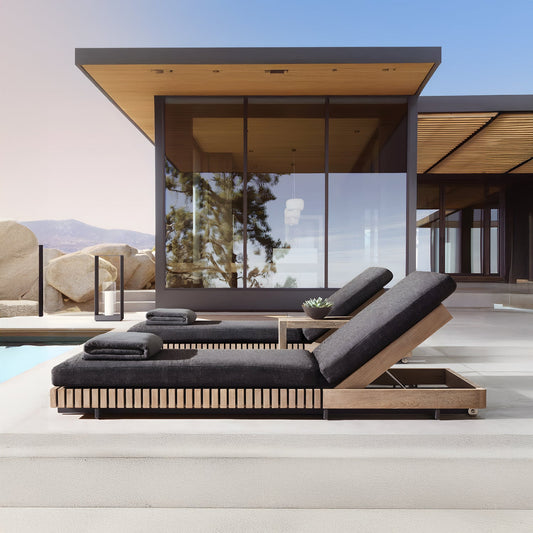 At a luxurious retreat, the Golden Coast Lounger Set by Landmark Decor graces the modern outdoor setting beside a shimmering pool. Facing a contemporary glass and wood building, clear skies and distant mountains enhance the serene ambiance of refined outdoor living.