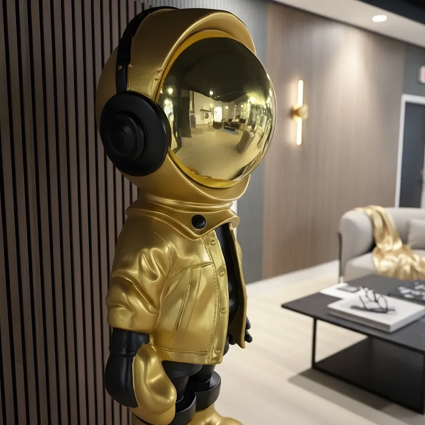 The Astronaut of the Stars by Landmark Decor, featuring a gold finish, reflective helmet, and headphones, stands in a modern living room, bringing artistic flair to neutral interior decor.