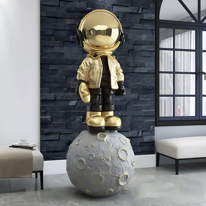 The Astronaut of the Stars by Landmark Decor—a gold astronaut statue with a jacket and headphones atop a detailed moon—brings striking, modern style to any living room with dark walls and large windows.