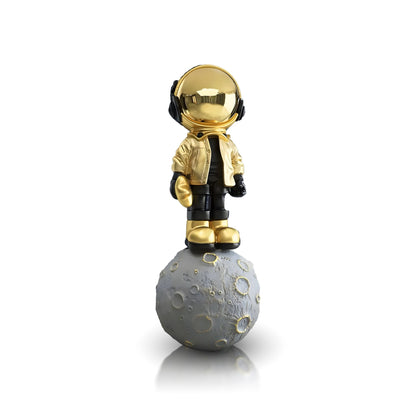 The Landmark Decor Astronaut of the Stars figurine features a gold and black astronaut standing on a gray, cratered moon—ideal for bringing artistic sculpture into your interior decor.