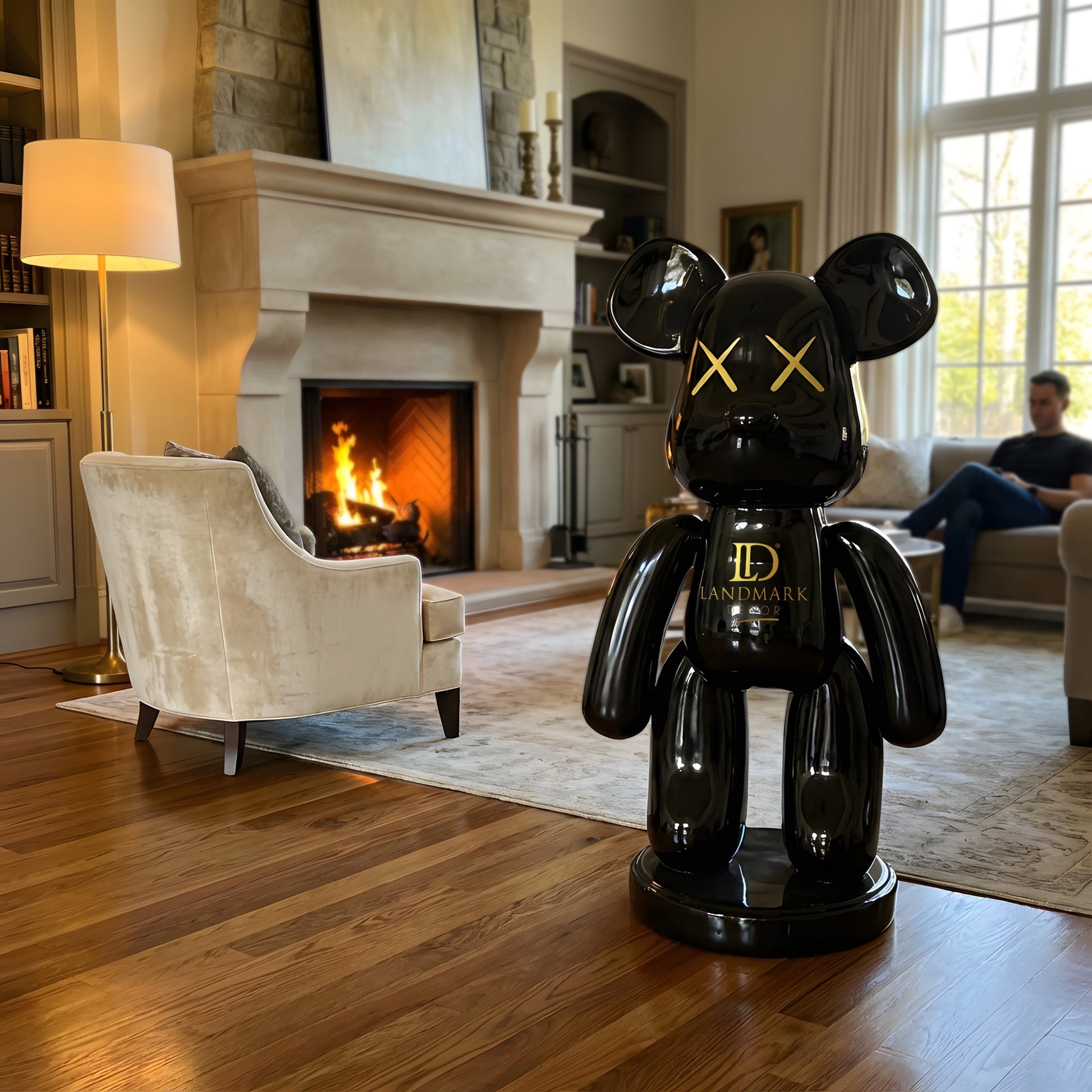 A Landmark Decor Black Bear - Medium sculpture stands as striking interior decor in a living room with a lit fireplace, while a man sits reading on the couch in the background.