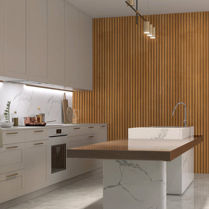 Modern kitchen with white cabinets, marble surfaces, a built-in oven, under-cabinet lighting, and a central island with sink. The wood slat accent wall features Landmark Decor's Natural Wood Color WPC Fluted Slat Wall Panel.